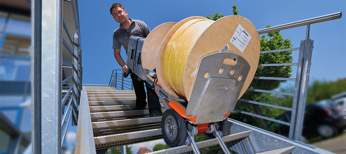 Ein Mann zieht eine Rolle Kabel mit einem Handwagen die Treppe hoch.