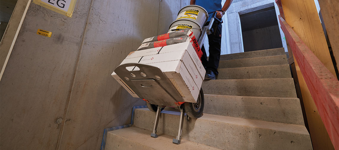 Ein Arbeiter schiebt eine Sackkarre mit Materialien die Treppe hoch.
