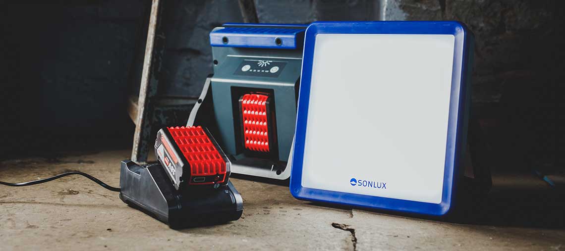 Ein roter Bosch Akku auf einer schwarzen Ladestation neben einem Scheinwerfer.