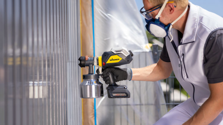 Ein Handwerker sprüht Farbe mit einer Wagner Spritzpistole auf eine Wand.