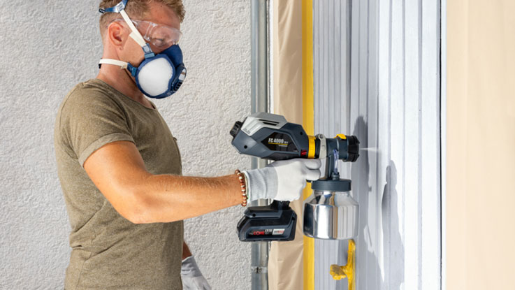 Mann sprüht Farbe mit Bosch Professional Sprayer an eine Wand.